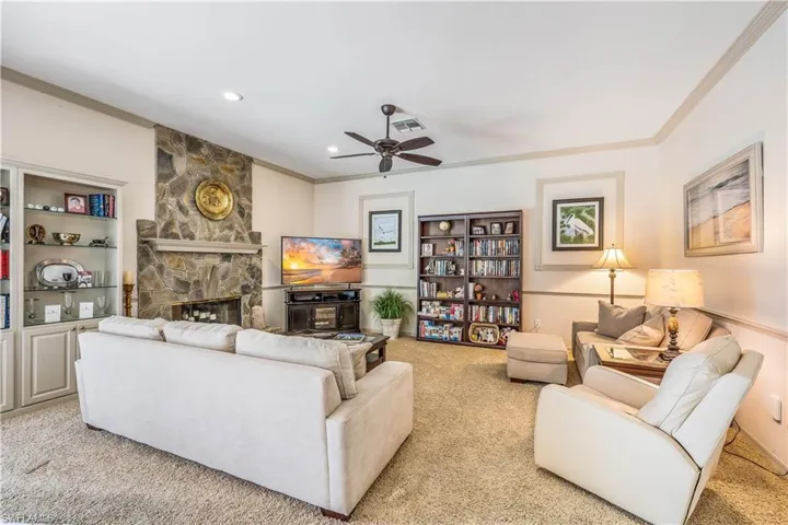 Family room featuring a fireplace, light carpet, built in shelves, and ceiling fan