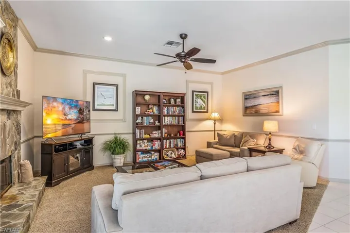 Tiled Family room with a stone fireplace, crown molding, and ceiling fan