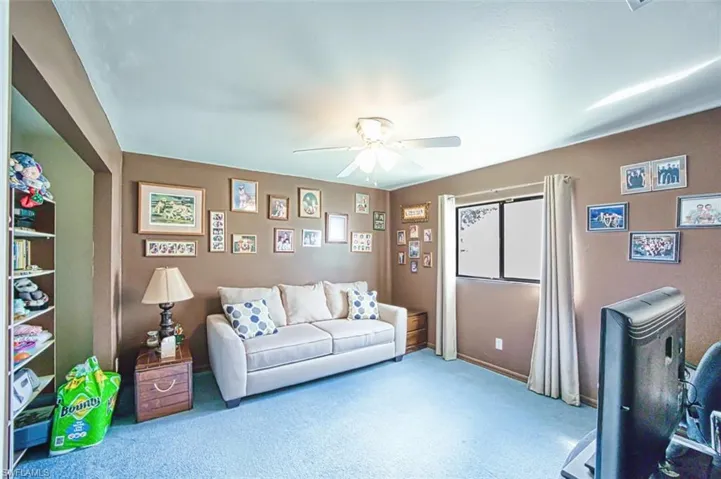 Carpeted living area featuring ceiling fan and baseboards