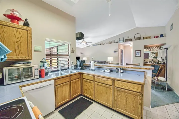 Kitchen featuring brown cabinets, vaulted ceiling, light tile patterned floors, a peninsula, and white appliances