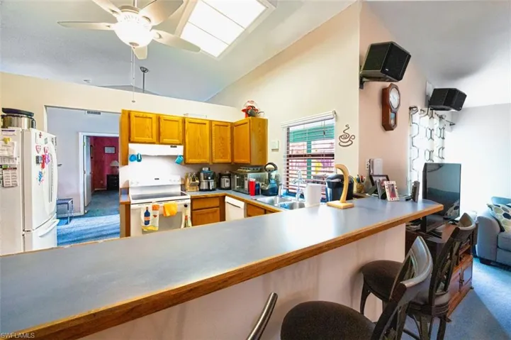 Kitchen with vaulted ceiling, brown cabinets, white appliances, dark carpet, and a skylight
