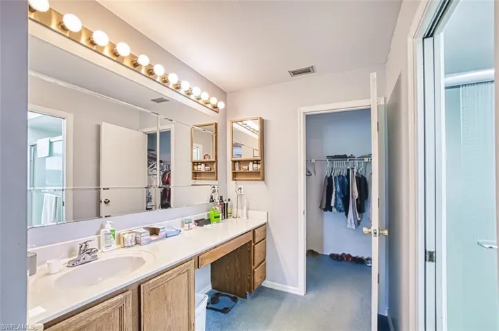 Full bath with a spacious closet, vanity, light colored carpet, and a shower with shower door