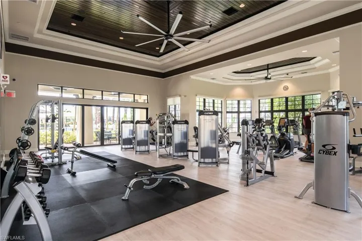 Gym featuring a raised ceiling, a ceiling fan, a high ceiling, crown molding, and wood finished floors