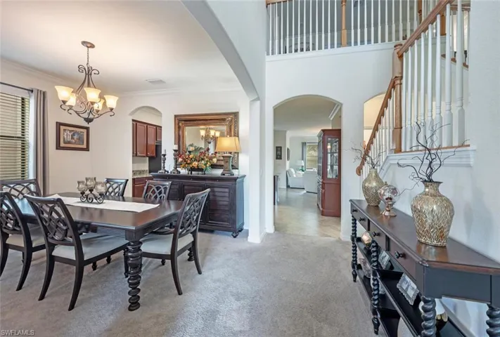 Dining room featuring a chandelier, arched walkways, ornamental molding, stairs, and light carpet