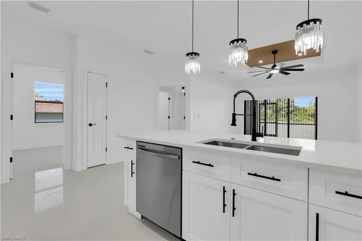 Kitchen with stainless steel dishwasher, light stone countertops, white cabinetry, hanging light fixtures, and ceiling fan