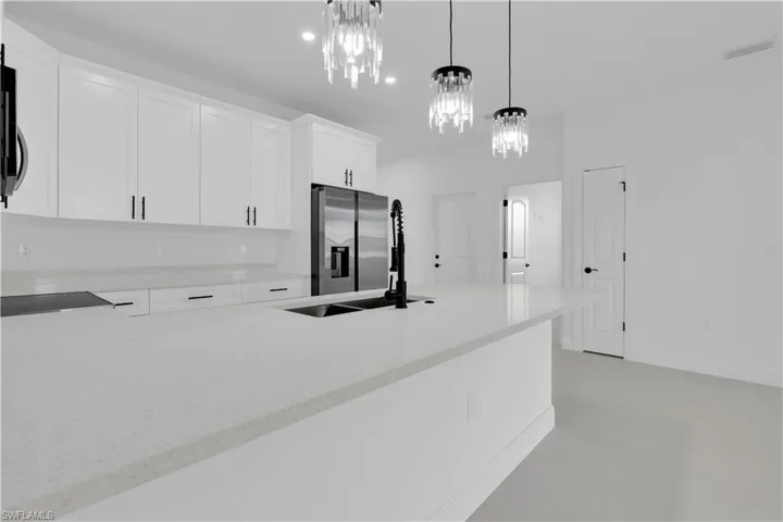 Kitchen with light stone countertops, white cabinetry, a peninsula, decorative light fixtures, and stainless steel fridge