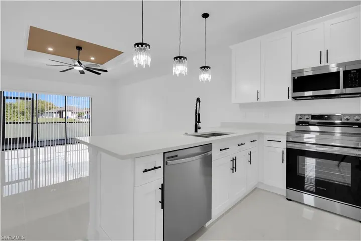 Kitchen featuring stainless steel appliances, a tray ceiling, white cabinets, pendant lighting, and recessed lighting