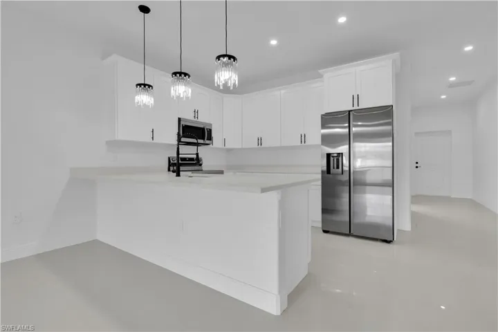 Kitchen featuring appliances with stainless steel finishes, white cabinetry, a peninsula, hanging light fixtures, and light tile patterned floors