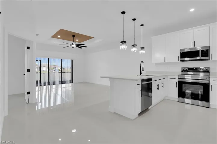 Kitchen featuring open floor plan, a raised ceiling, stainless steel appliances, white cabinets, and recessed lighting