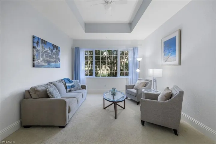 Carpeted living room with ceiling fan and a raised ceiling