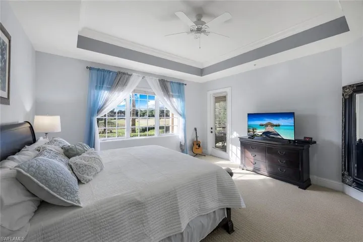Bedroom with access to exterior, ceiling fan, a tray ceiling, light carpet, and ornamental molding