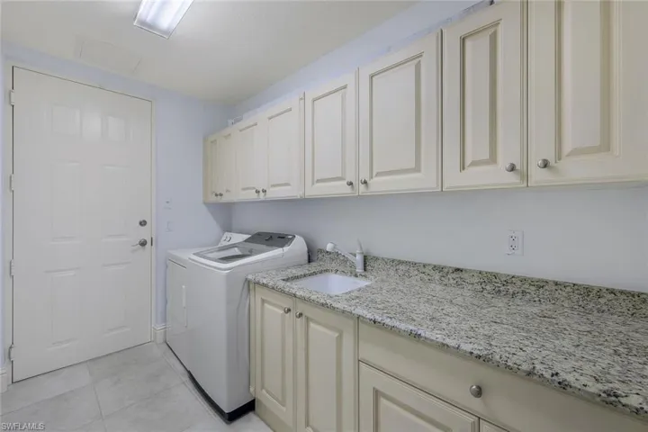Laundry room with washing machine and dryer, sink, light tile patterned flooring, and cabinets