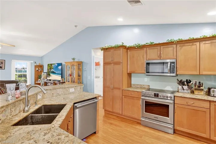 Kitchen with appliances with stainless steel finishes, vaulted ceiling, light wood-type flooring, light stone countertops, and washer / clothes dryer