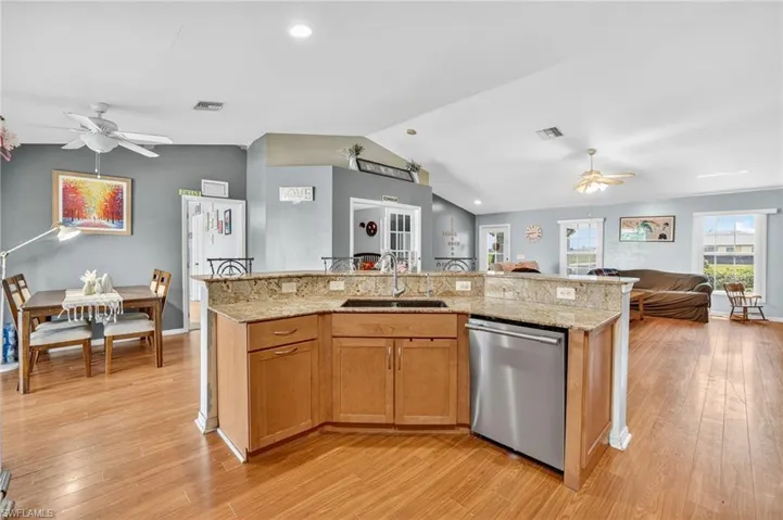 Kitchen with ceiling fan, lofted ceiling, open floor plan, stainless steel dishwasher, and light wood-style flooring