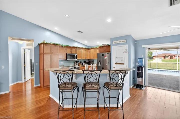 Kitchen featuring vaulted ceiling, light wood finished floors, a breakfast bar area, stainless steel appliances, and light stone countertops