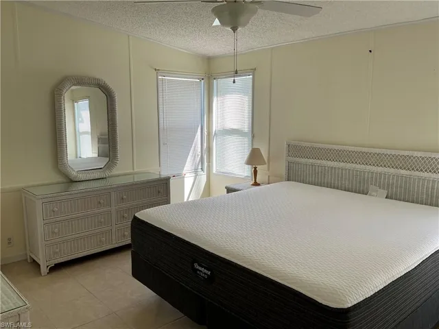 Bedroom with a decorative wall, multiple windows, a textured ceiling, a ceiling fan, and light tile patterned floors