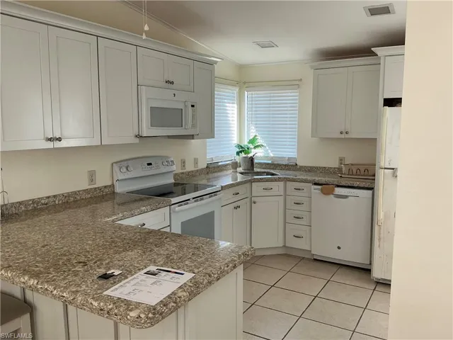 Kitchen featuring white appliances, a peninsula, white cabinetry, light tile patterned flooring, and lofted ceiling
