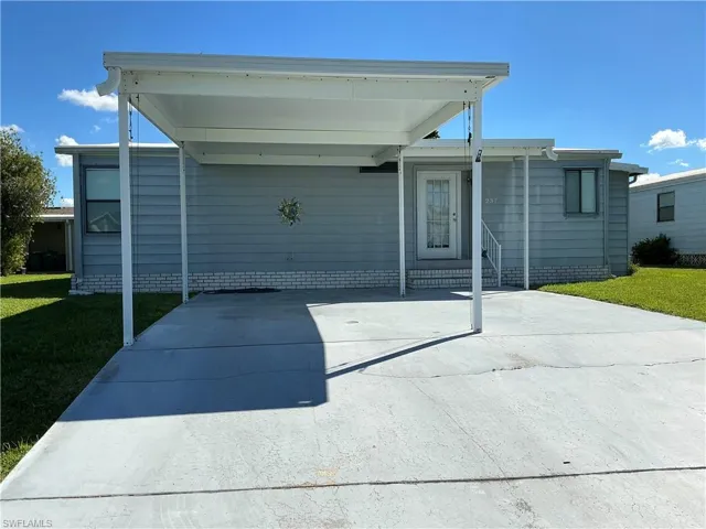 View of front of home with a front yard, concrete driveway, a patio, and a carport