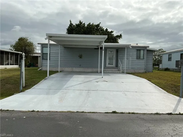 Manufactured / mobile home featuring a front lawn, concrete driveway, entry steps, and a carport