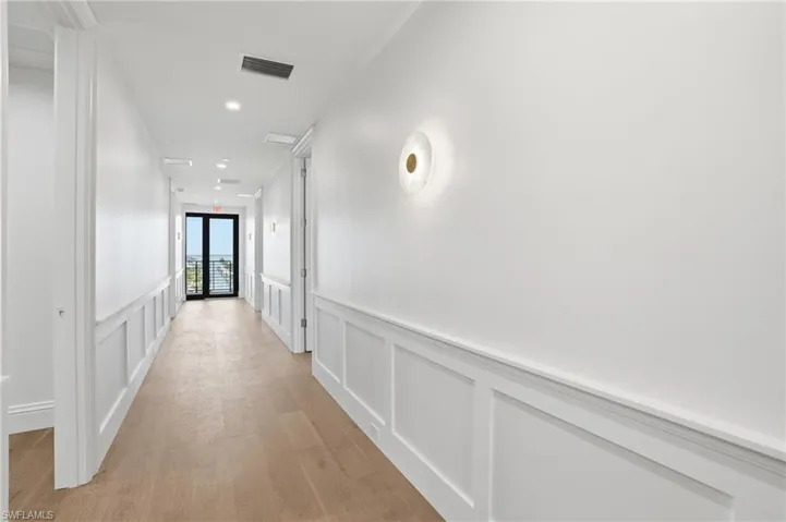 Hall featuring a decorative wall, light wood-type flooring, wainscoting, and recessed lighting