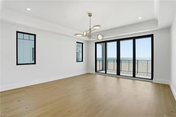 Empty room with a raised ceiling, a chandelier, light wood-type flooring, a water view, and ornamental molding