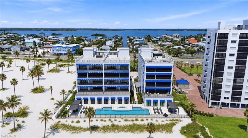 Coastal condominium architecture with multiple private balconies, a resort-style swimming pool, surrounding sandy beach, and mature palm trees - Virtually Edited Image