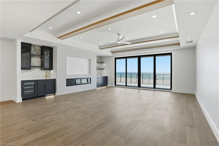 Unfurnished living room featuring light wood-type flooring, a ceiling fan, beamed ceiling, recessed lighting, and a tray ceiling