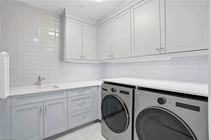 Laundry area featuring washer and clothes dryer, light tile patterned floors, cabinet space, and tile walls