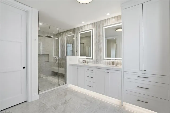 Full bath with double vanity, a shower stall, recessed lighting, and light marble finish floors