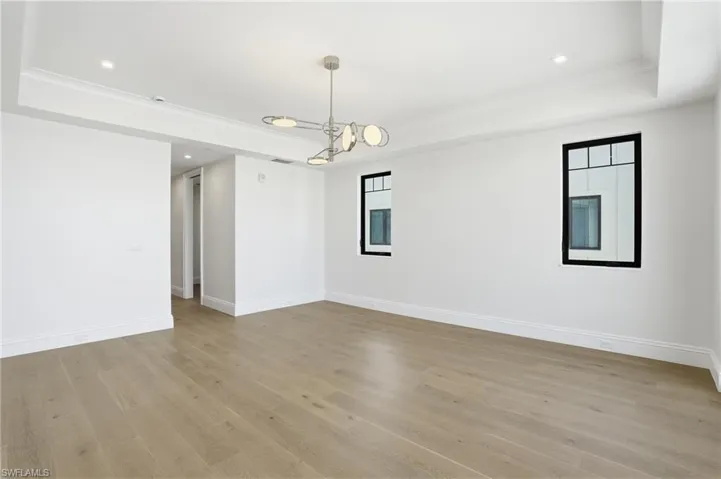 Unfurnished room featuring a raised ceiling, recessed lighting, light wood finished floors, and ornamental molding
