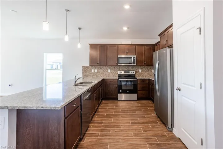 Kitchen with sink, appliances with stainless steel finishes, decorative backsplash, decorative light fixtures, and kitchen peninsula