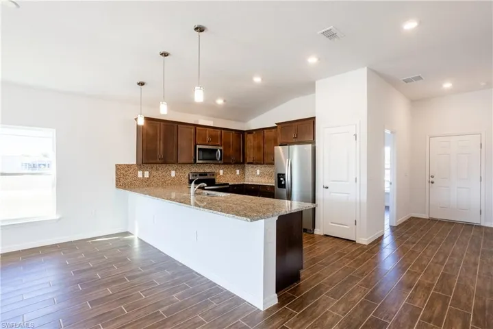 Kitchen featuring pendant lighting, dark wood-type flooring, stainless steel appliances, light stone counters, and kitchen peninsula