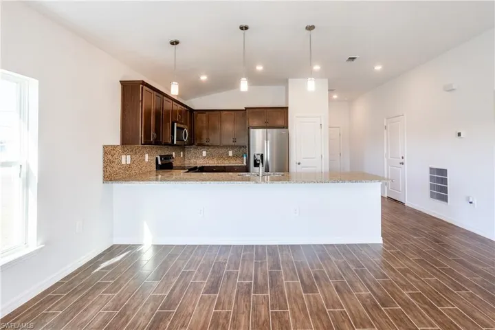 Kitchen featuring tasteful backsplash, hanging light fixtures, dark hardwood / wood-style floors, stainless steel appliances, and light stone countertops