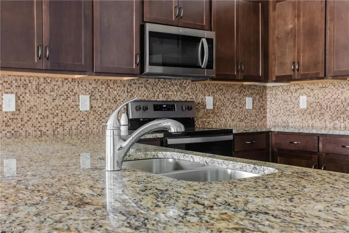 Kitchen with dark brown cabinetry, sink, light stone counters, appliances with stainless steel finishes, and decorative backsplash