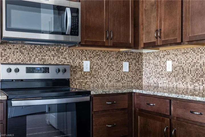Kitchen with tasteful backsplash, dark brown cabinetry, stainless steel appliances, and light stone countertops