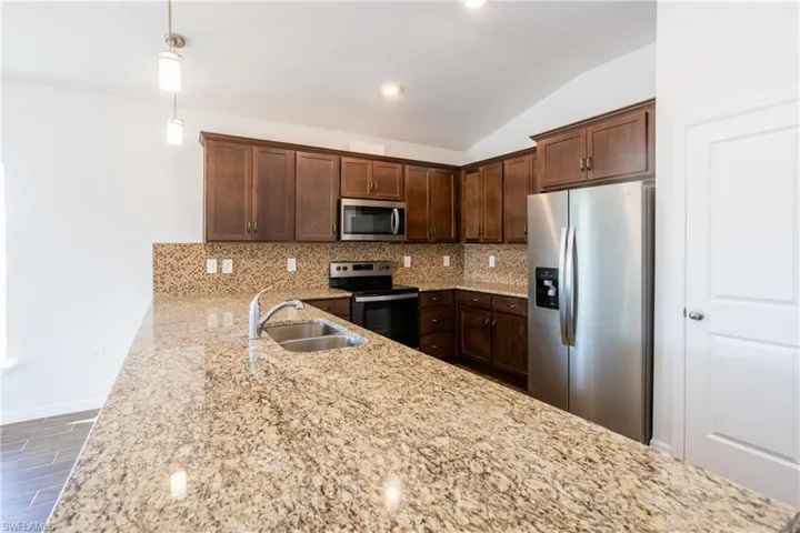 Kitchen featuring appliances with stainless steel finishes, decorative light fixtures, sink, backsplash, and light stone counters