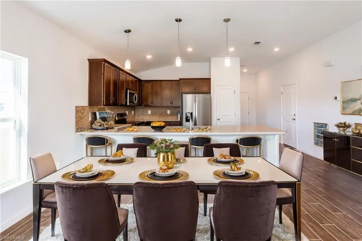 Kitchen with hardwood / wood-style flooring, stainless steel appliances, decorative backsplash, decorative light fixtures, and vaulted ceiling