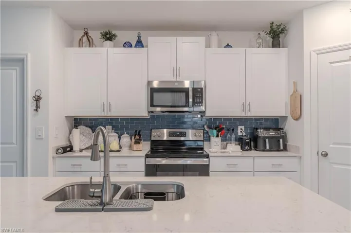 Kitchen with appliances with stainless steel finishes, white cabinetry, tasteful backsplash, and light stone countertops