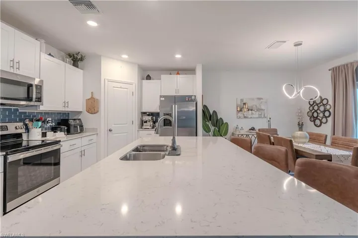 Kitchen featuring appliances with stainless steel finishes, white cabinetry, decorative light fixtures, backsplash, and light stone countertops