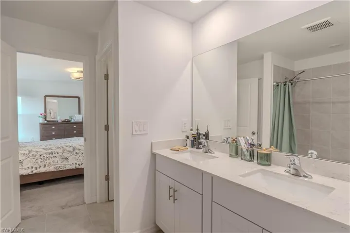Ensuite bathroom featuring double vanity, a shower with curtain, and light tile patterned flooring