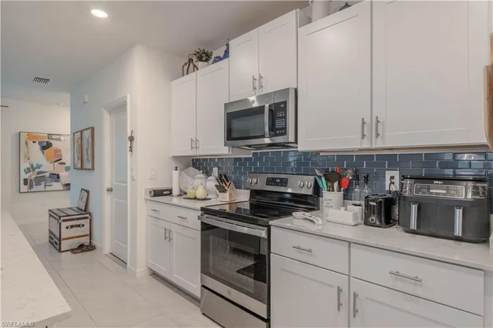Kitchen featuring appliances with stainless steel finishes, light stone countertops, white cabinets, backsplash, and recessed lighting