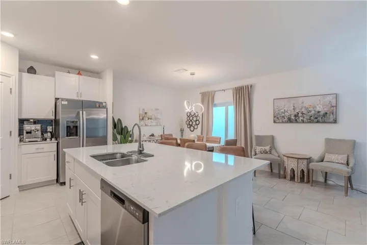 Kitchen with white cabinets, appliances with stainless steel finishes, pendant lighting, light stone countertops, and light tile patterned floors