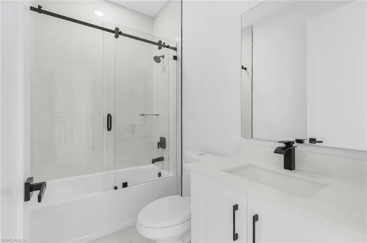 Full bath featuring bath / shower combo with glass door, vanity, and light tile patterned floors