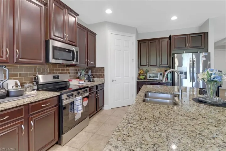 Kitchen featuring appliances with stainless steel finishes, light tile patterned floors, light stone countertops, decorative backsplash, and a sink