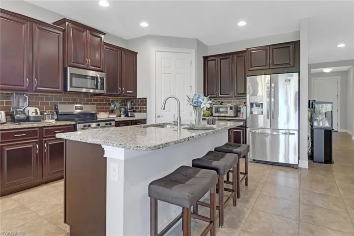 Kitchen with a sink, appliances with stainless steel finishes, a center island with sink, backsplash, and light stone counters