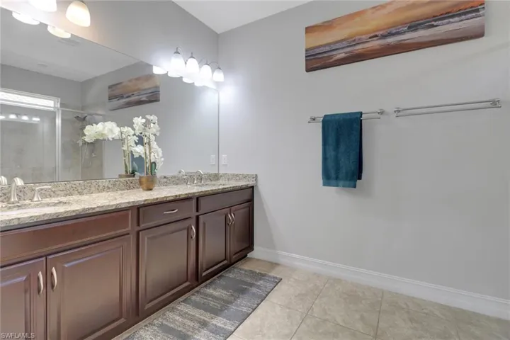 Full bath with baseboards, a sink, double vanity, tile patterned floors, and a stall shower