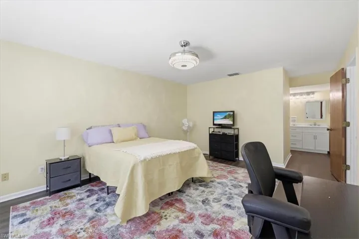 Spacious room featuring wood-finish flooring, a contemporary ceiling light fixture, and an en-suite bathroom with a double vanity and framed mirror