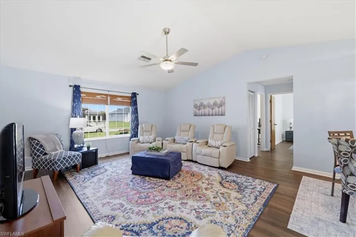 Spacious living area featuring wood-finish flooring, vaulted ceilings, and a ceiling fan with integrated lighting