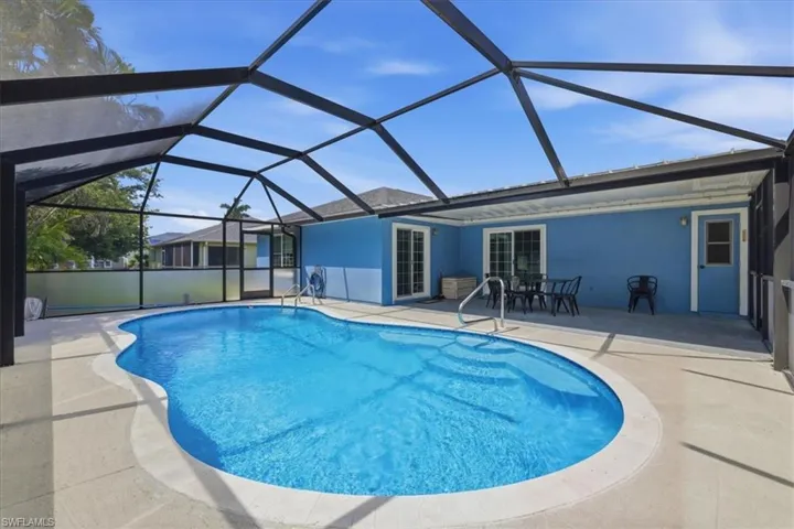 Screen-enclosed pool deck featuring a freeform swimming pool with integrated steps, ample surrounding patio space, and direct access to the vibrant blue exterior of the property via multiple sliding glass doors and an additional side door