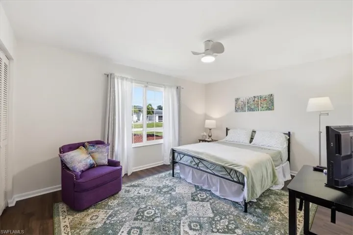 Bedroom featuring wood-finish flooring, a double window with white trim, a ceiling fan with integrated lighting, and louvered bifold closet doors